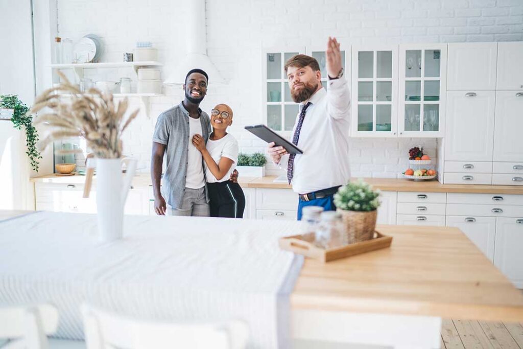 A couple reviewing documents with a real estate agent at a dining room table in a residential home.